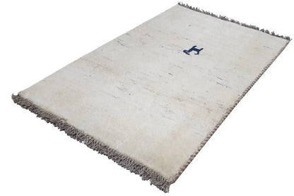 Cream-colored Gabbeh rug, laid diagonally, dark fringes, blue decorative motif