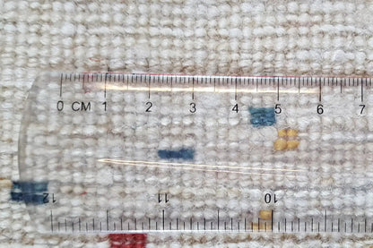 Close-up of a Gabbeh rug with measuring tape on a woven, light-colored textured surface