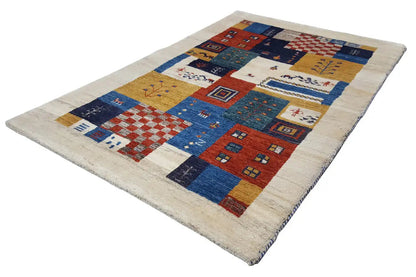 Gabbeh rug at an angle: geometric patchwork in blue, red, and beige on a light background