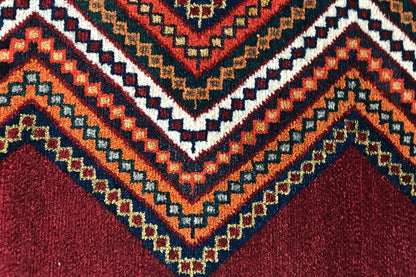 Gabbeh rug detail: multicolored zigzag border and diamonds on a reddish-brown background
