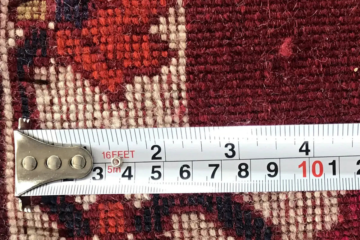 Gabbeh rug with tape measure along the edge, reddish-brown grid pattern