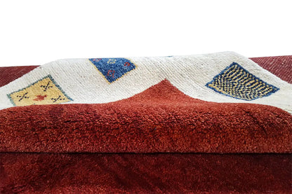 Gabbeh rug: detailed view of the dense pile, red background with beige decorative motifs.