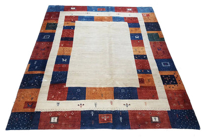 Gabbeh rug with a light central field and a geometric patchwork border in blue, red, and orange