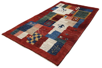 Rug with a red border and patchwork-style patterns in blue, green, and beige, at an angle