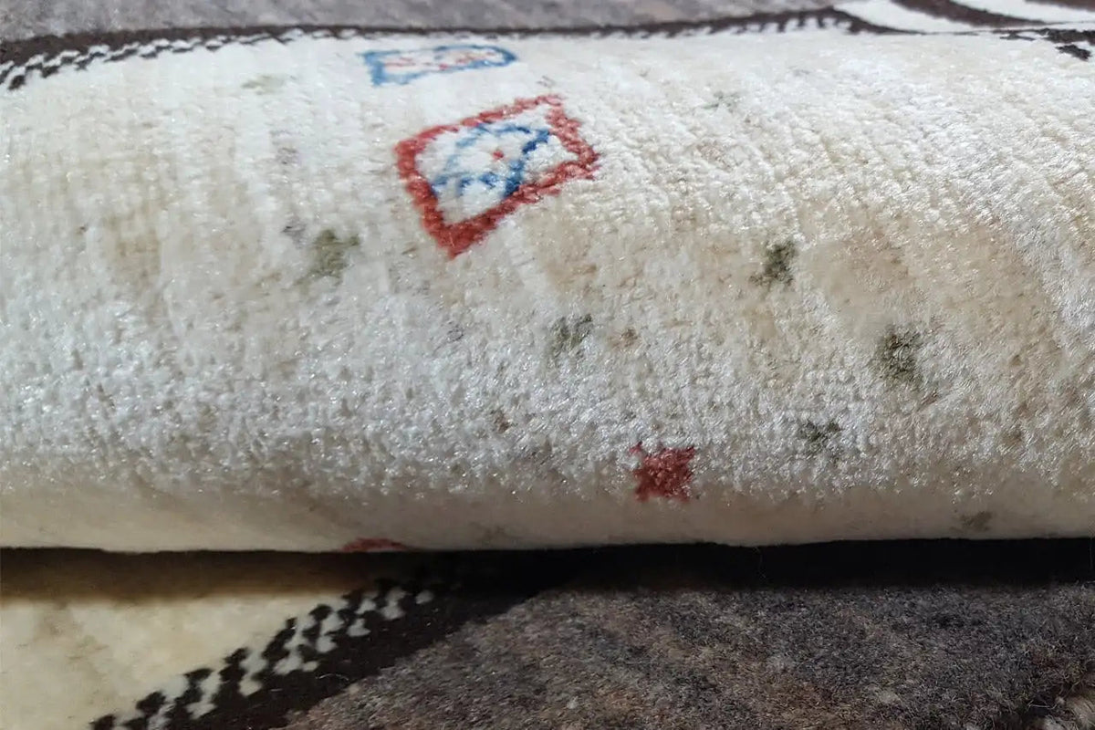 Close-up of a Gabbeh rug: cream-colored pile with small red and blue motifs