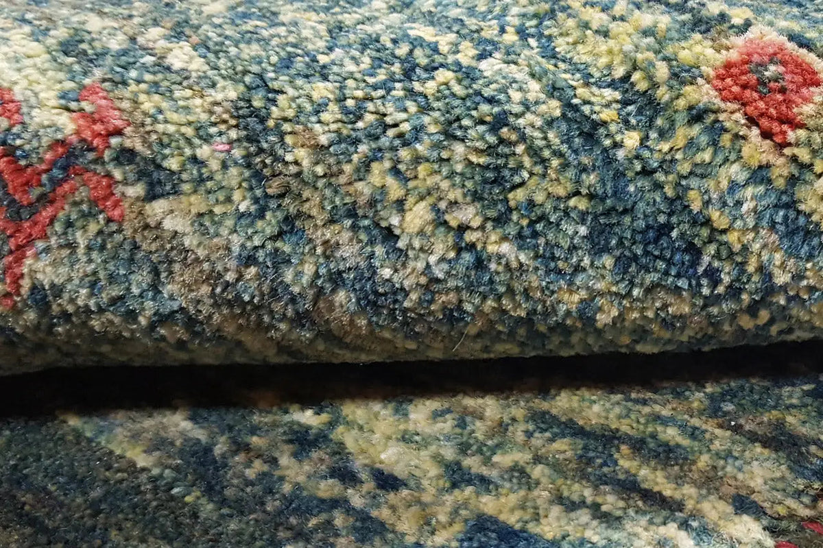 Close-up of a Gabbeh rug: dense pile in shades of blue and green with red decorative motifs.