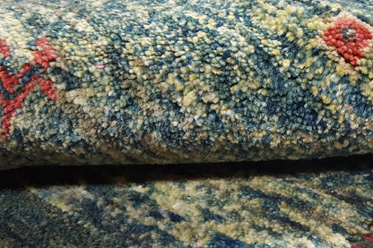 Close-up of a Gabbeh rug: dense pile in shades of blue and green with red decorative motifs.