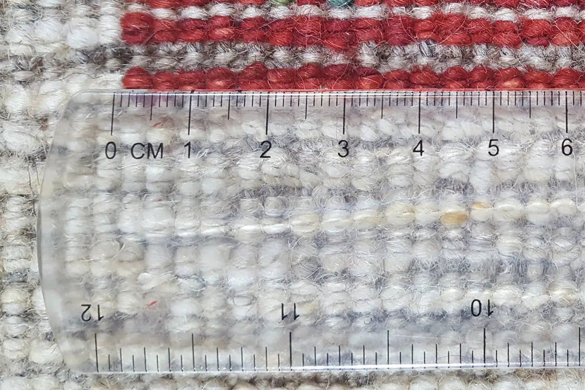 Gabbeh rug detail, pile height with measuring tape: cream-colored pile with a red border