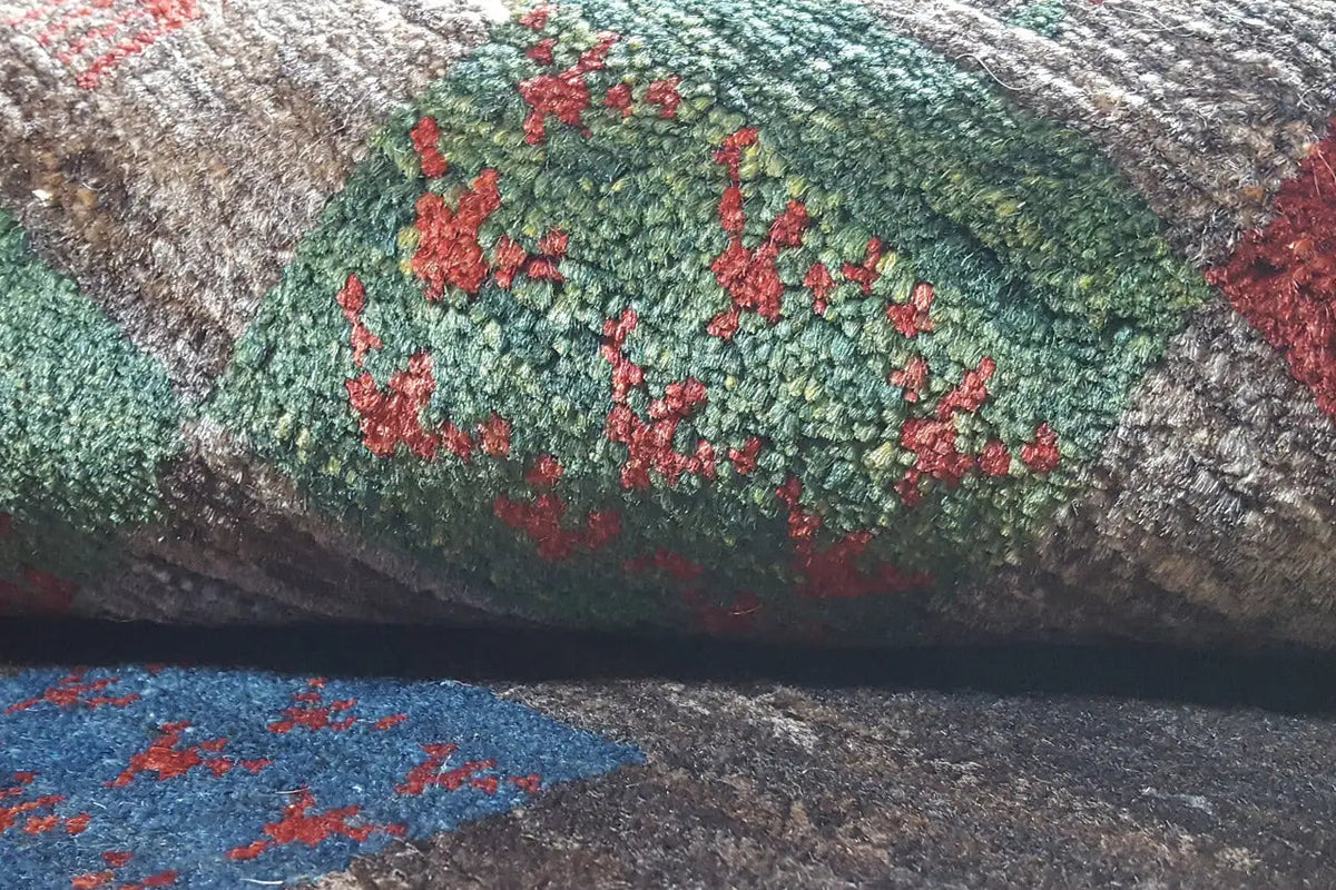 Close-up of a Gabbeh rug: floral patchwork motifs in green and red on a gray background