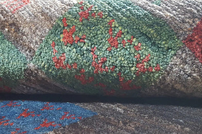 Close-up of a Gabbeh rug: floral patchwork motifs in green and red on a gray background