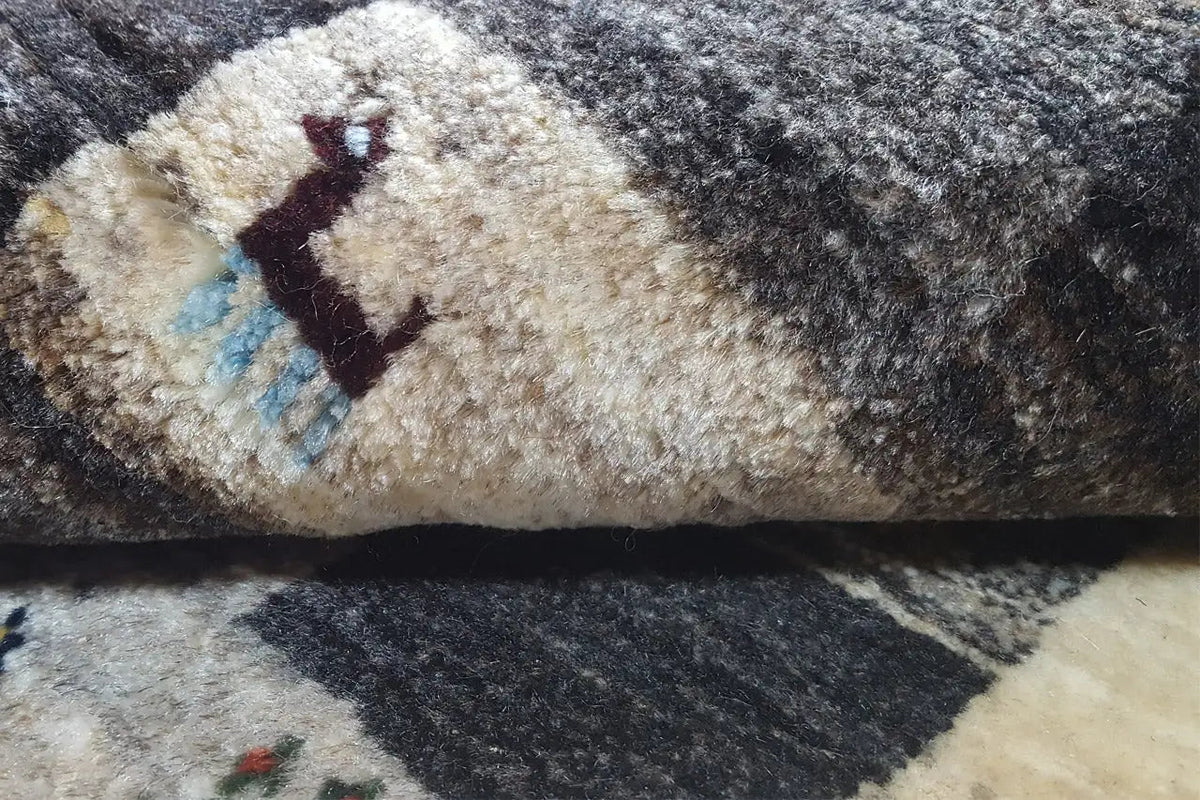 Close-up of a Gabbeh rug: dense pile with patterned stripes in blue, gray, and beige