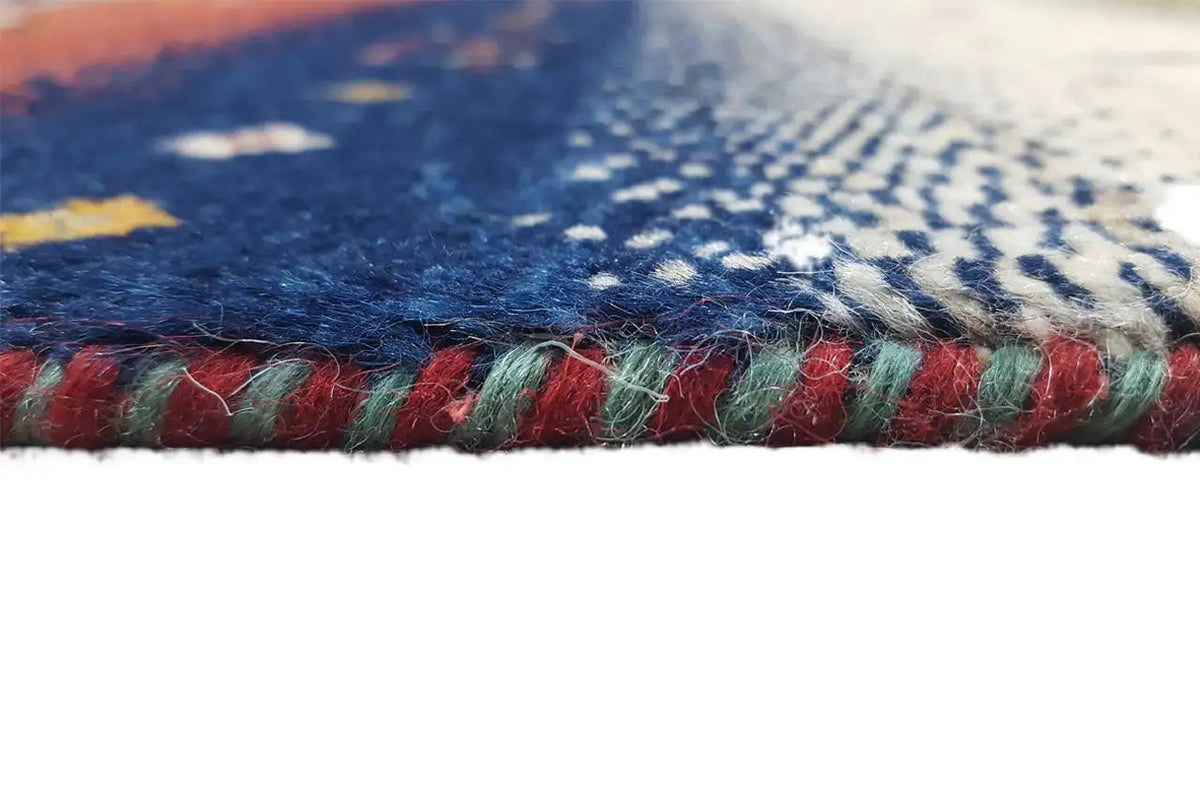 Gabbeh rug with a multicolored selvedge and fringes along the bottom edge.