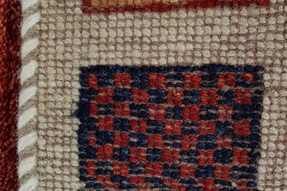 Rug detail with beige fabric and a dark blue-red square pattern, finished with fringes