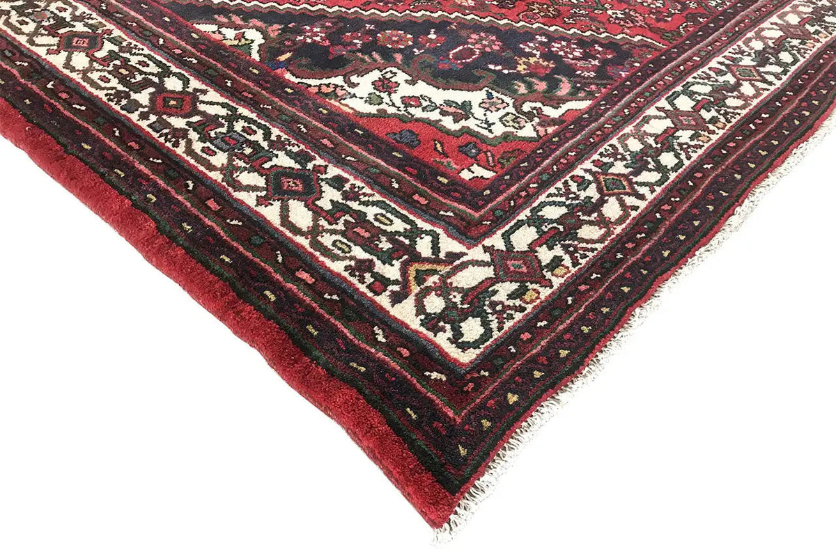 Corner of a rug with a red background, cream-colored ornamental elements, and a dark border