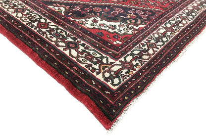Corner of a rug with a red background, cream-colored ornamental elements, and a dark border