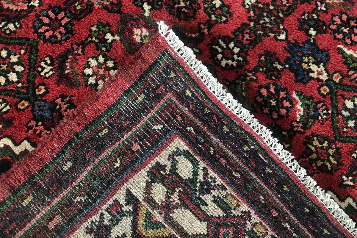 Close-up of the carpet corner: red pattern, greenish-blue border stripes, and cream ornaments