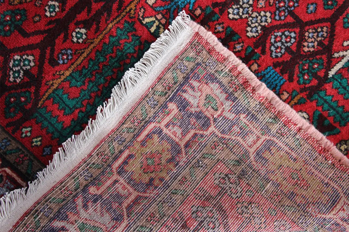 Hamadan runner detail: hemmed edge with fringes and a patterned area in shades of red.