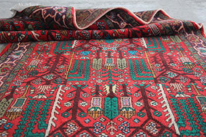Hamadan rug laid out: red pattern with turquoise and green elements, with fringes.