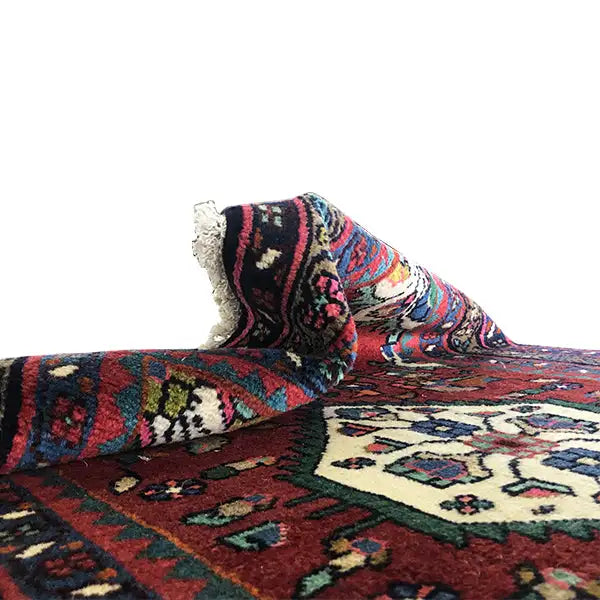 Folded Oriental rug with fringes, red background, and colorful ornamental pattern