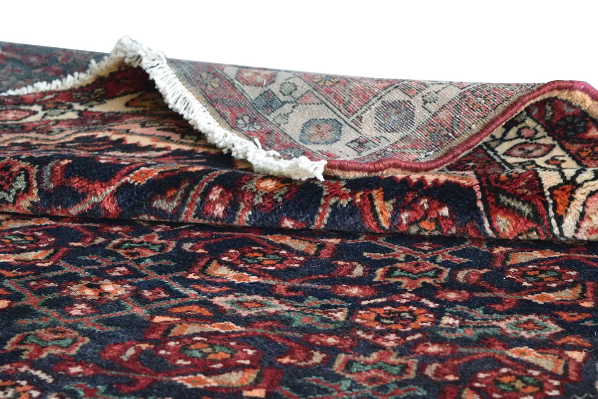Oriental rug runner with rounded pile and a white border, dark blue-red pattern folded crosswise.