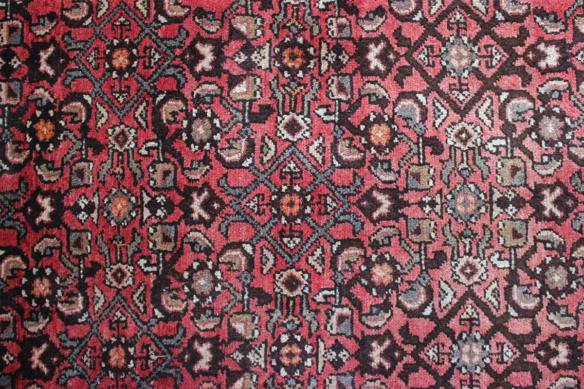 Close-up of carpet surface: red sections with black, beige, and cream-colored patterns