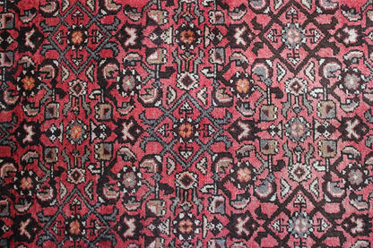 Close-up of carpet surface: red sections with black, beige, and cream-colored patterns
