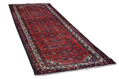 Long, narrow Oriental rug runner with a red background pattern and multicolored border