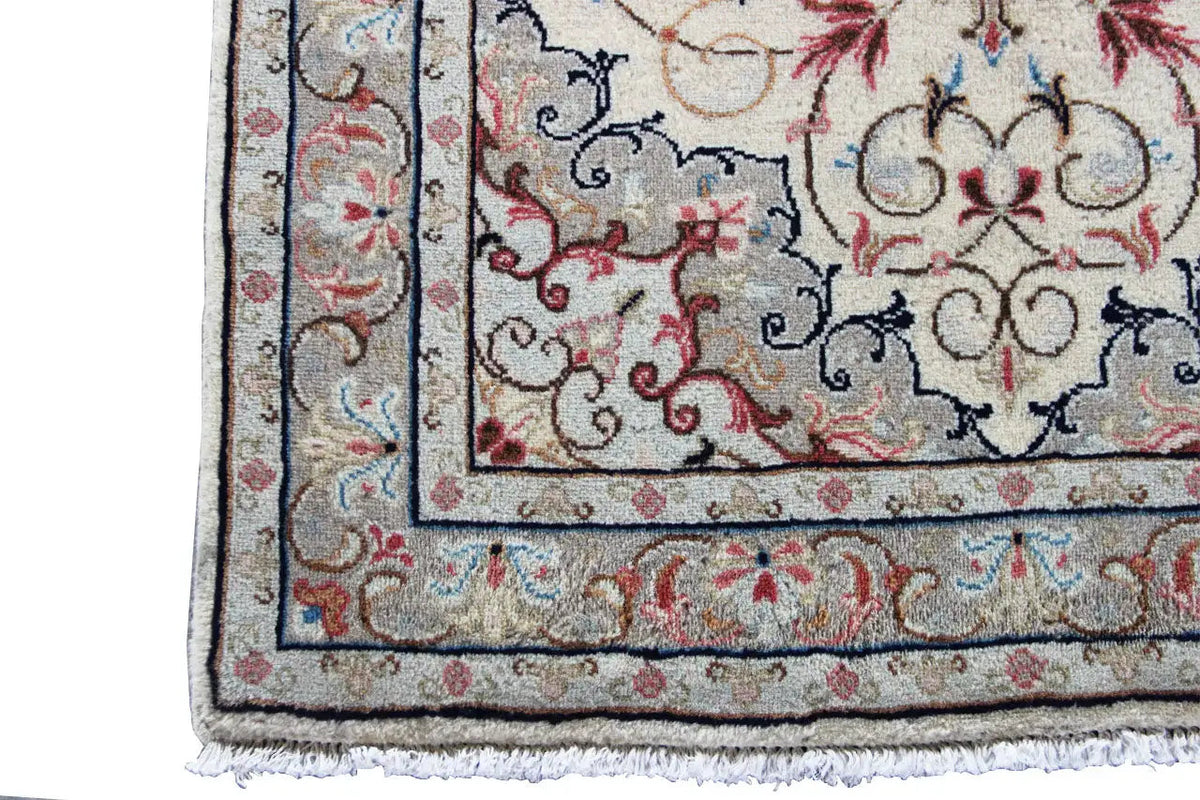 Close-up detail of a beige Oriental rug with a blue border, red decorations, and fringe