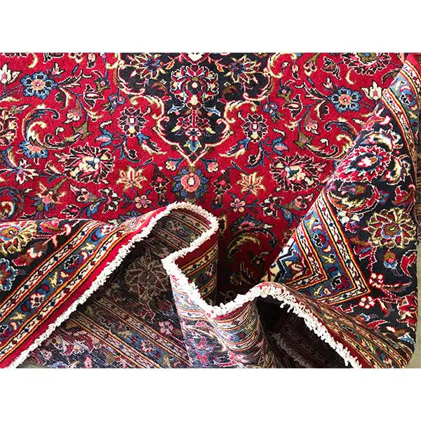 Keshan rug with a red floral pattern, folded corner, and frayed edge