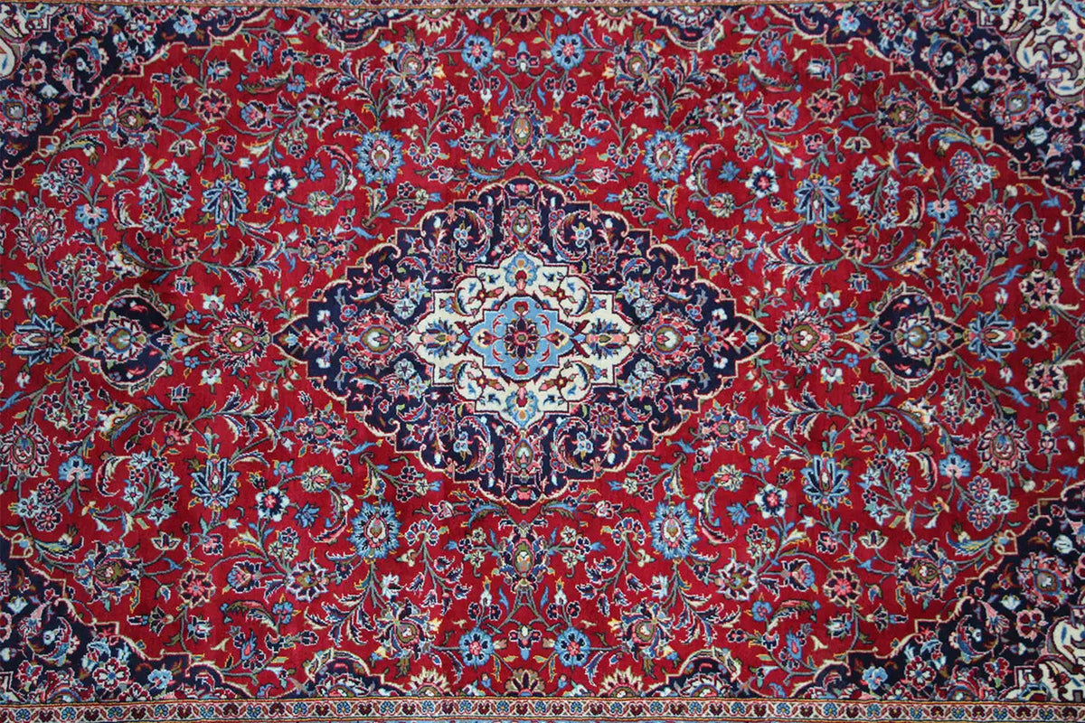 Rust-red Keshan rug with a dense paisley and floral pattern in the center.
