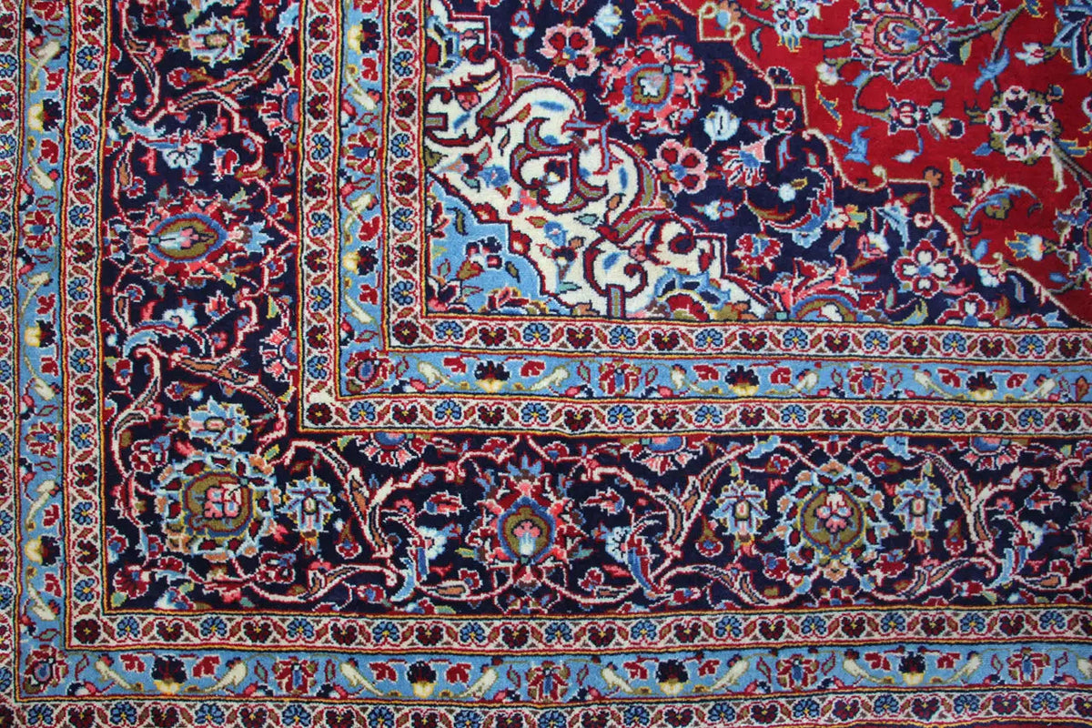 Corner detail of the Keshan rug: multicolored border with ornamental bands on red.