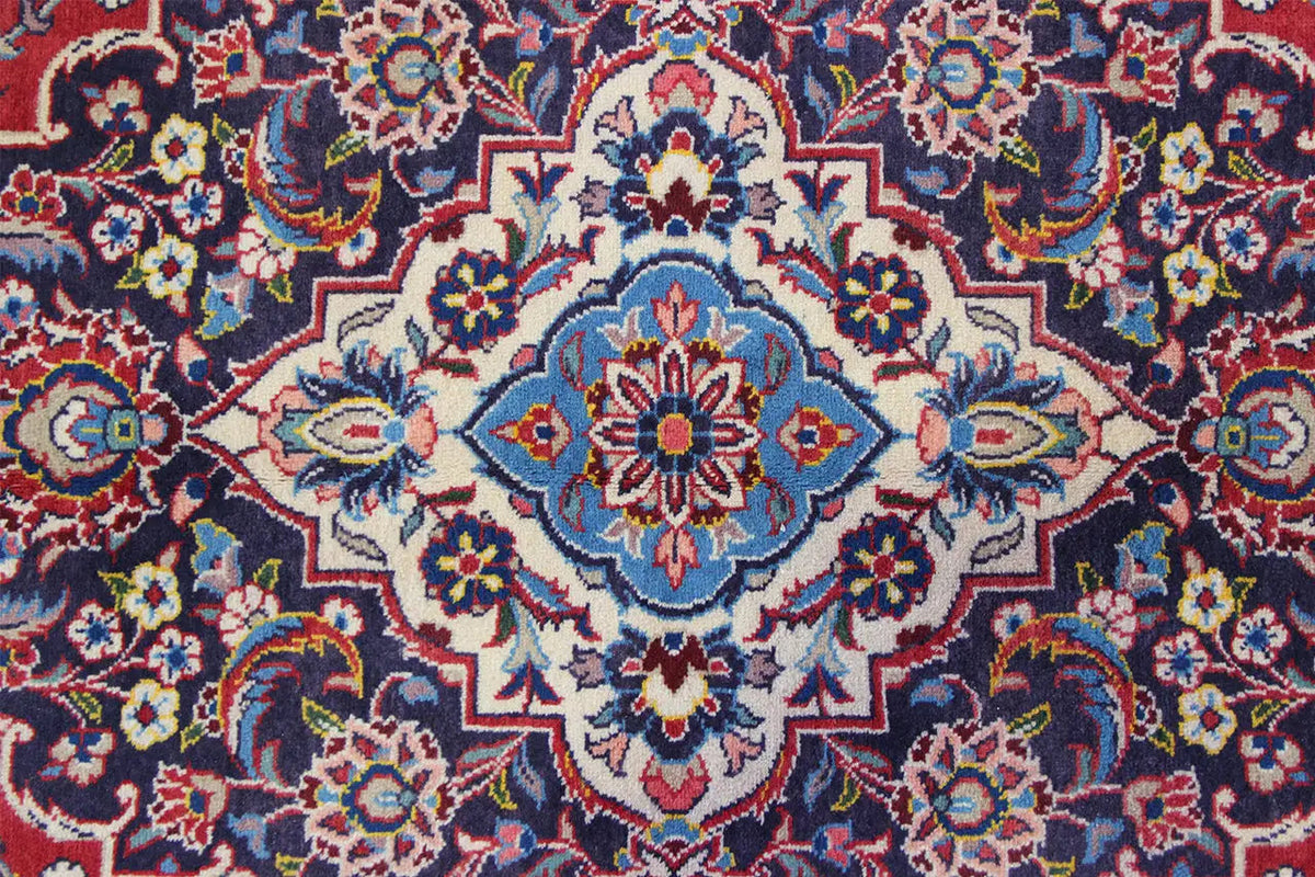 Keshan carpet with a central medallion featuring blue and red floral ornaments, densely patterned.