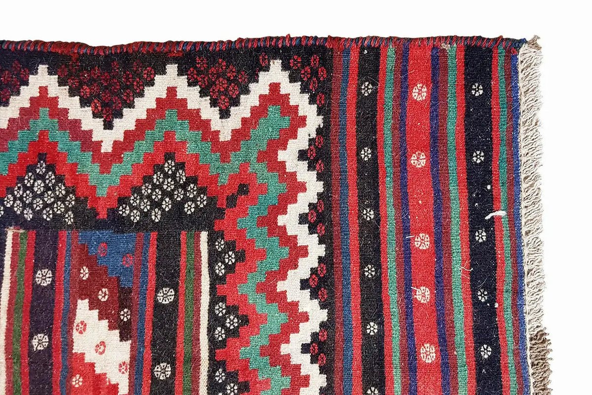 Kilim rug with fringed edges; zigzag and diamond patterns in red, green, black, and white.