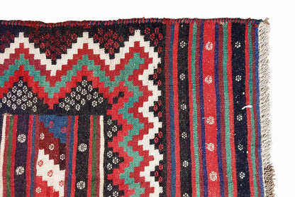 Kilim rug with fringed edges; zigzag and diamond patterns in red, green, black, and white.