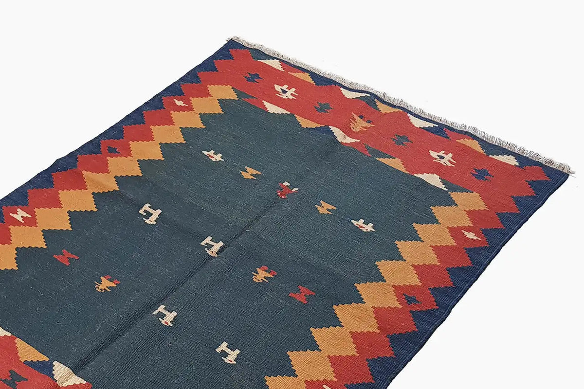 Close-up of a kilim rug: blue field with rows of symbols and a red border around the edge