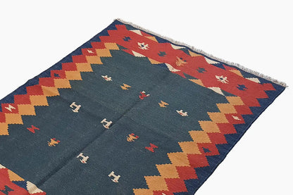 Close-up of a kilim rug: blue field with rows of symbols and a red border around the edge