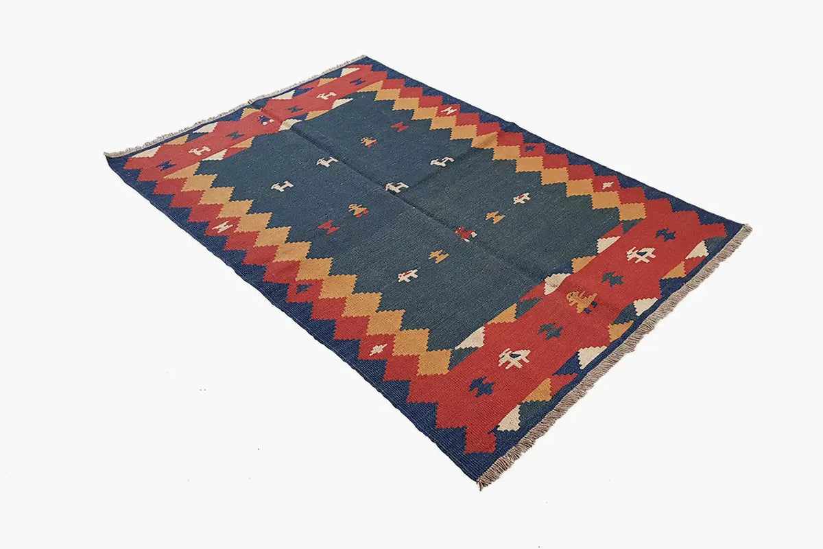 Kilim rug with a blue background and a multicolored border of zigzags and geometric shapes