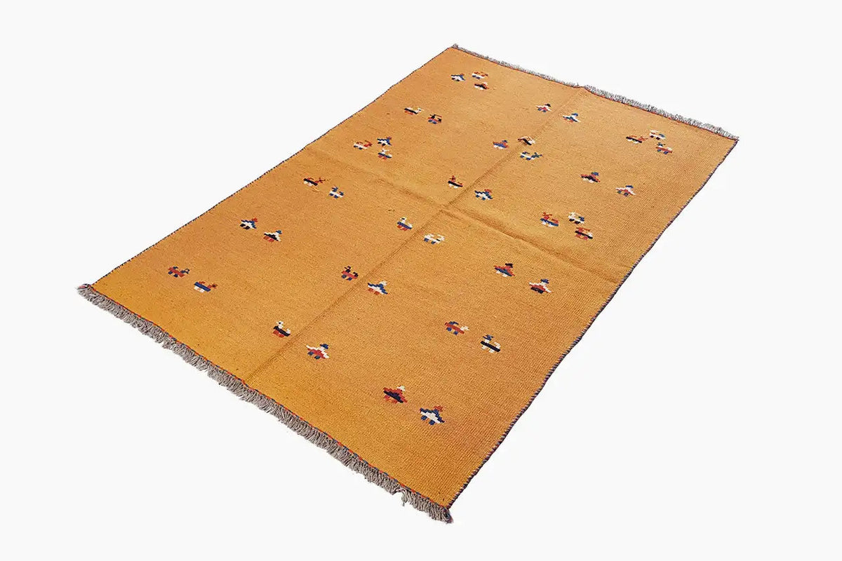 Ochre-brown kilim rug, spread out at an angle, with colorful patterns and fringes