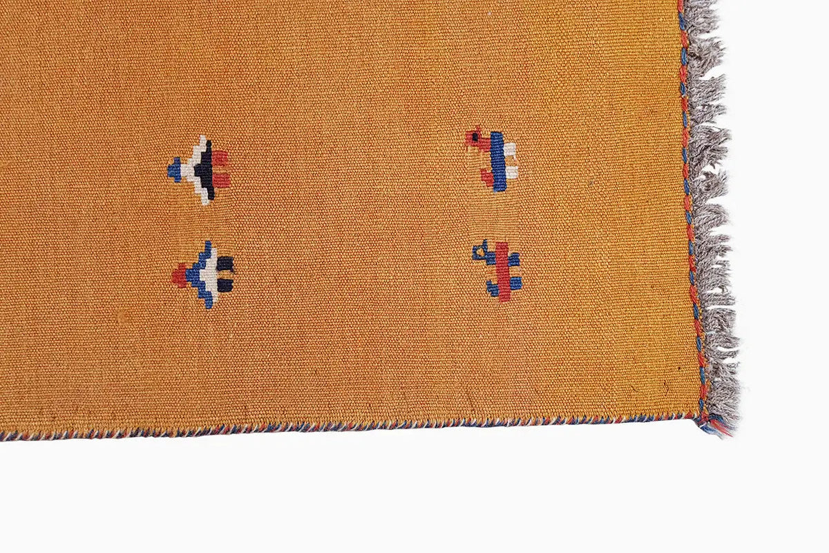 Ochre-brown kilim rug corner with multicolored patterns and fringes