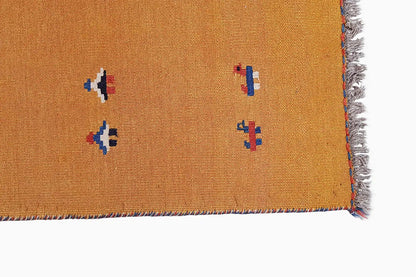 Ochre-brown kilim rug corner with multicolored patterns and fringes
