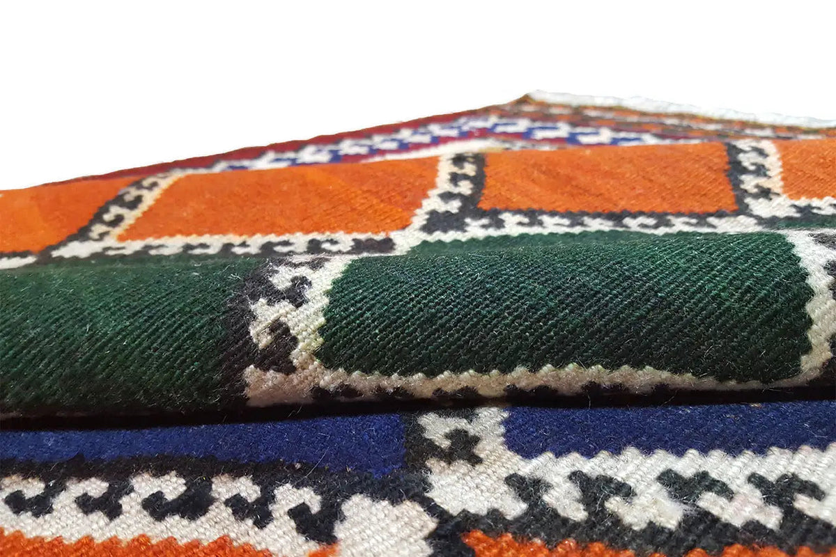 Close-up of a kilim rug: colorful diamonds over a woven pile, with fringes