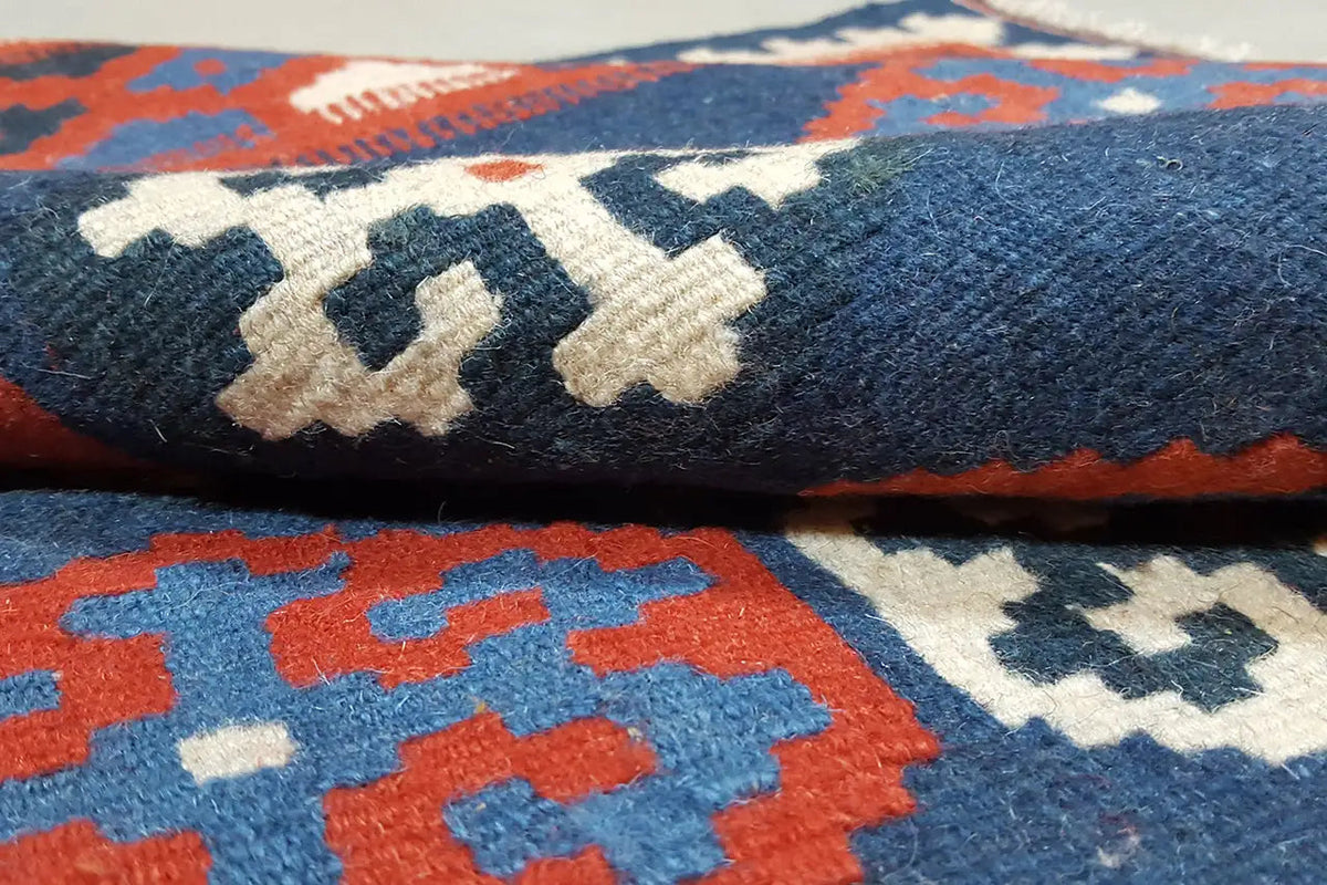 Close-up of a kilim rug: woven pile with geometric motifs in blue, red, and white