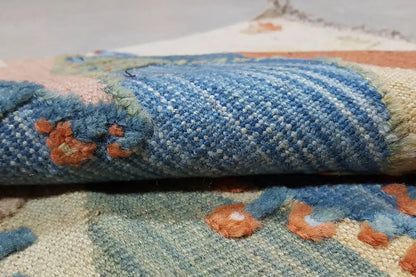 Kilim rug fold with a dense woven structure, blue segment, and relief-like fringe along the edge