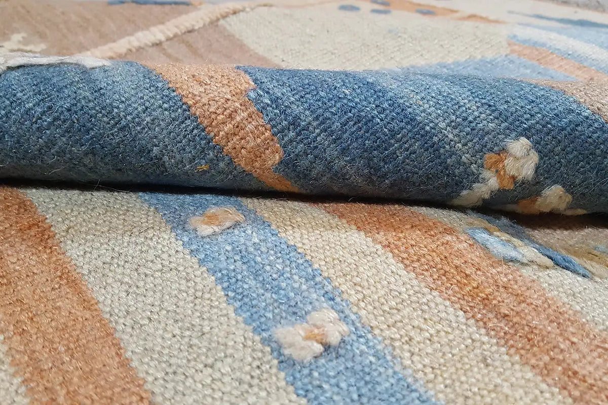 Kilim textile in detail: coarse fabric with blue-beige stripes and orange-brown areas.