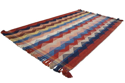 Flat-lay rug with a zigzag pattern in red, blue, and cream, corner tassels.