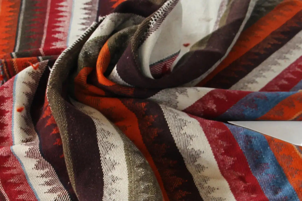 Close-up of a Jajim rug with folds, featuring stripes in brown, red, beige, and blue