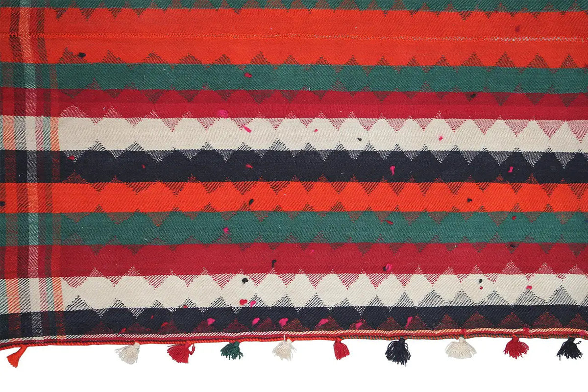 Close-up of a jajim rug with patterned areas, a surrounding border with tassels and fringes.