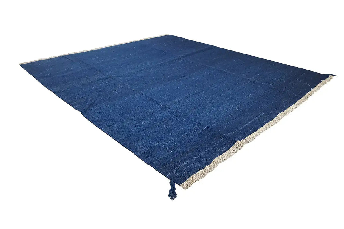 Blue kilim rug laid diagonally, with a beige border and fringes
