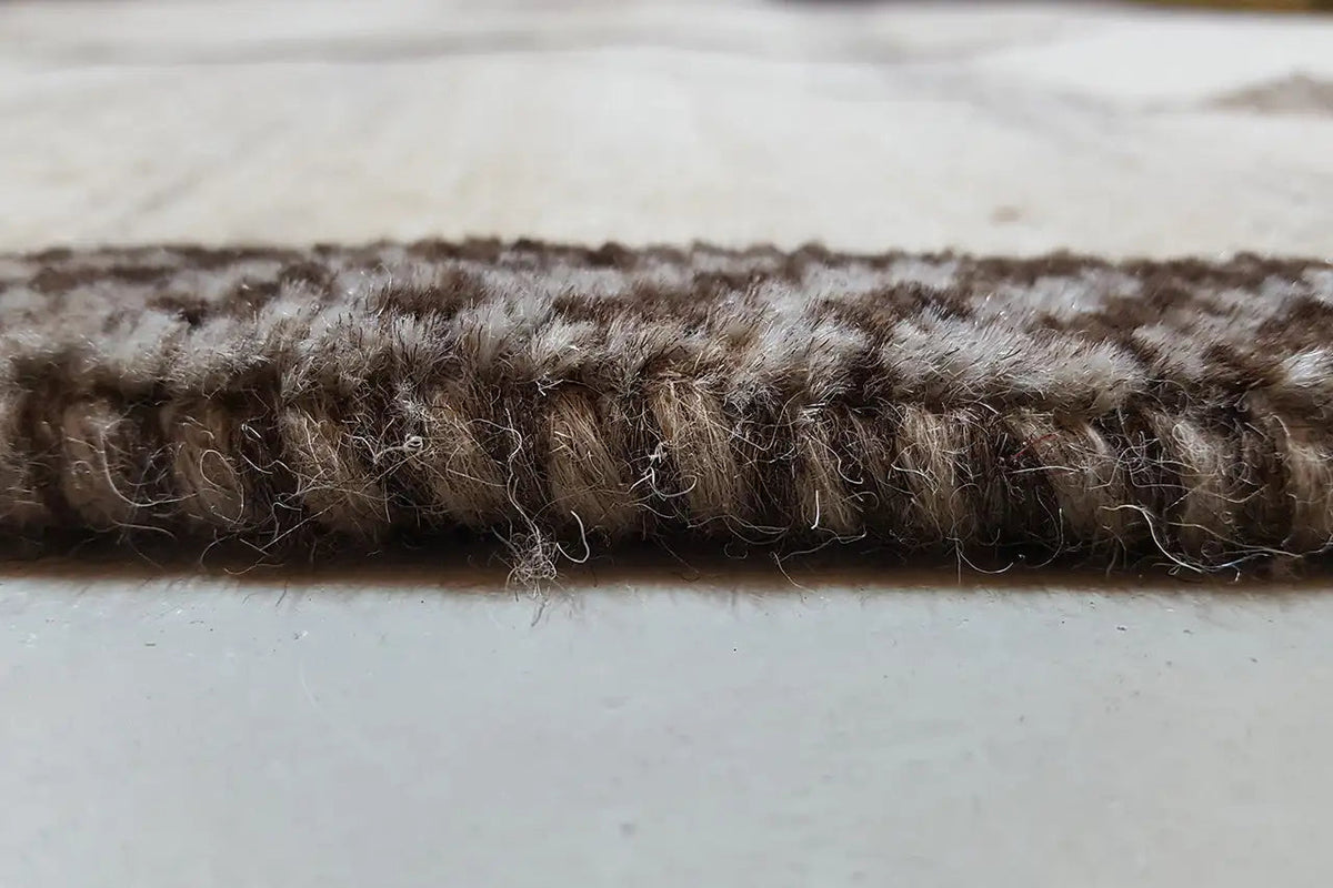 Close-up of the carpet edge: short, dense pile in dark brown on a light background