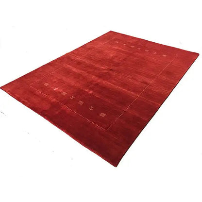 Red Gabbeh rug, shown rolled up, with a decorative border and small symbolic patterns